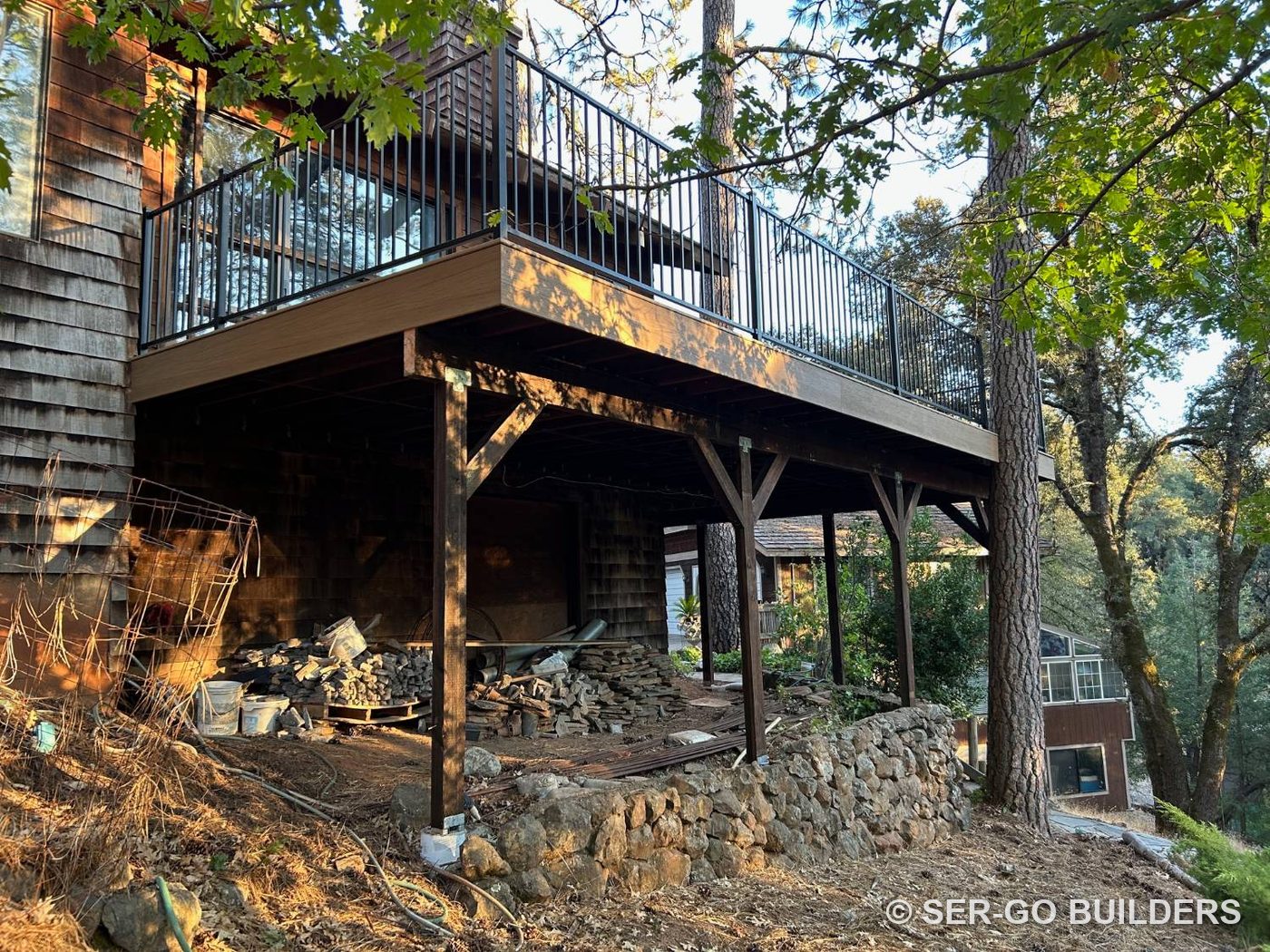 Elevated composite deck with steel railing on braced posts above a stone retaining wall