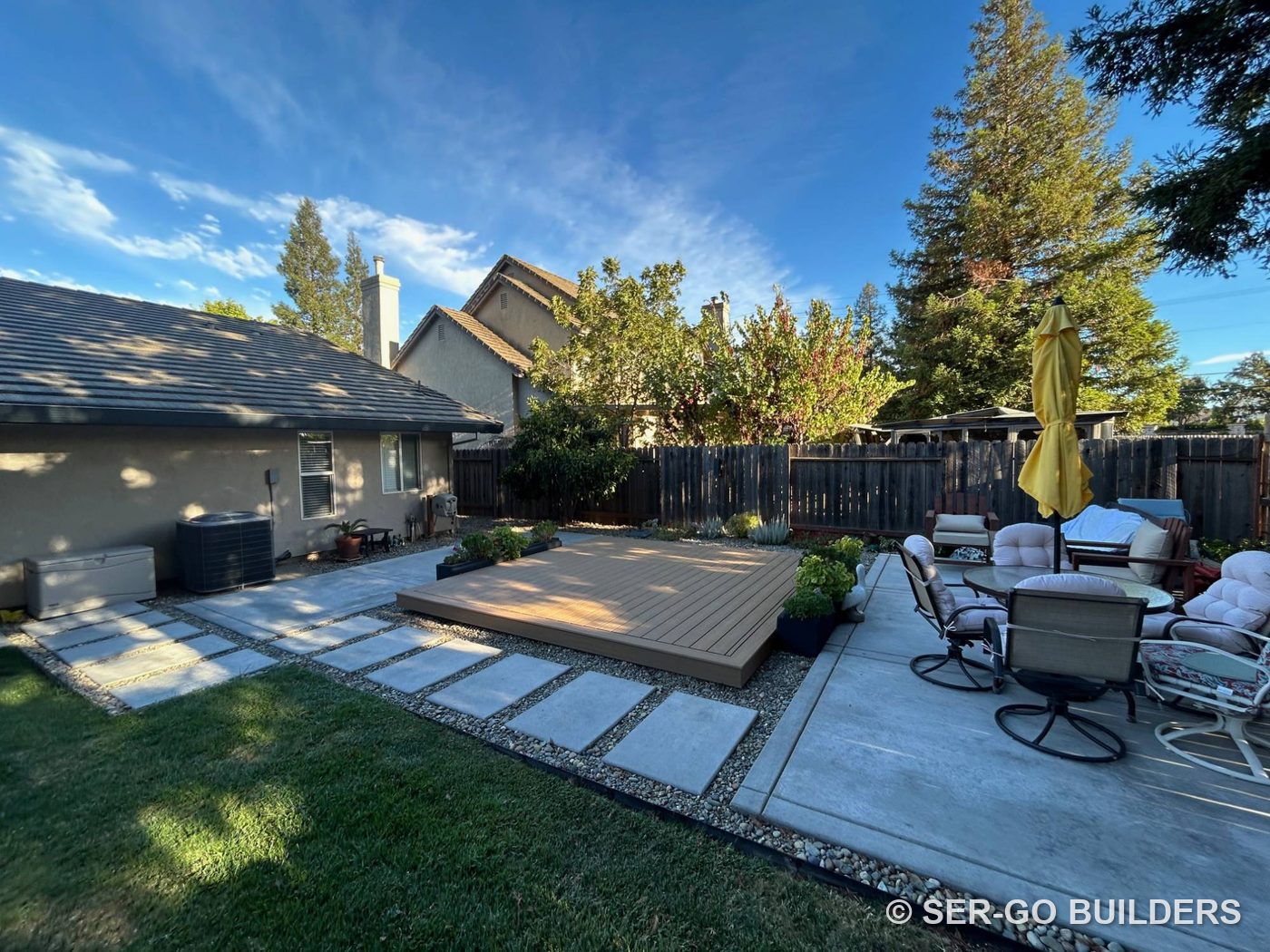 Low composite platform deck set in river rock between concrete patios and stepping stones