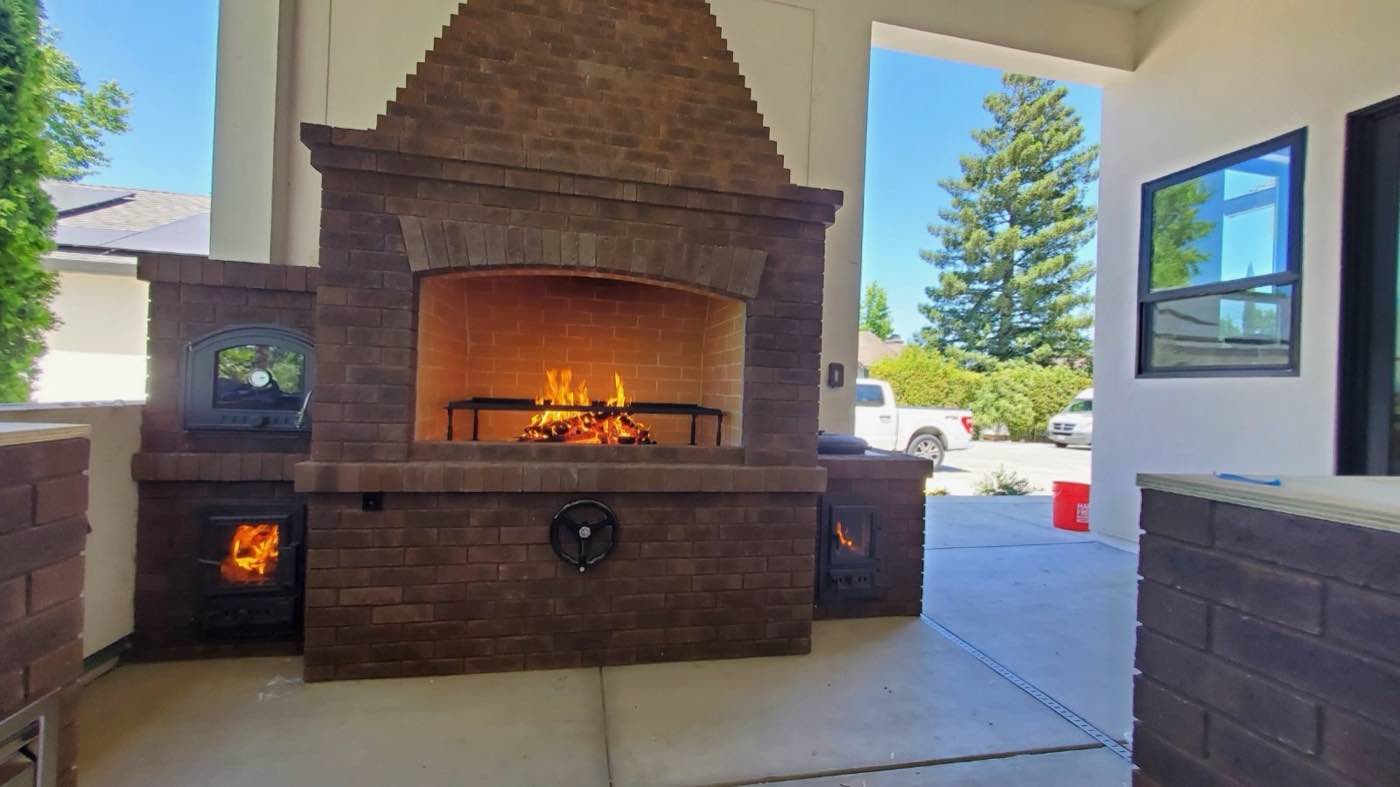 Finished outdoor brick fireplace with a fire lit and a built-in pizza oven