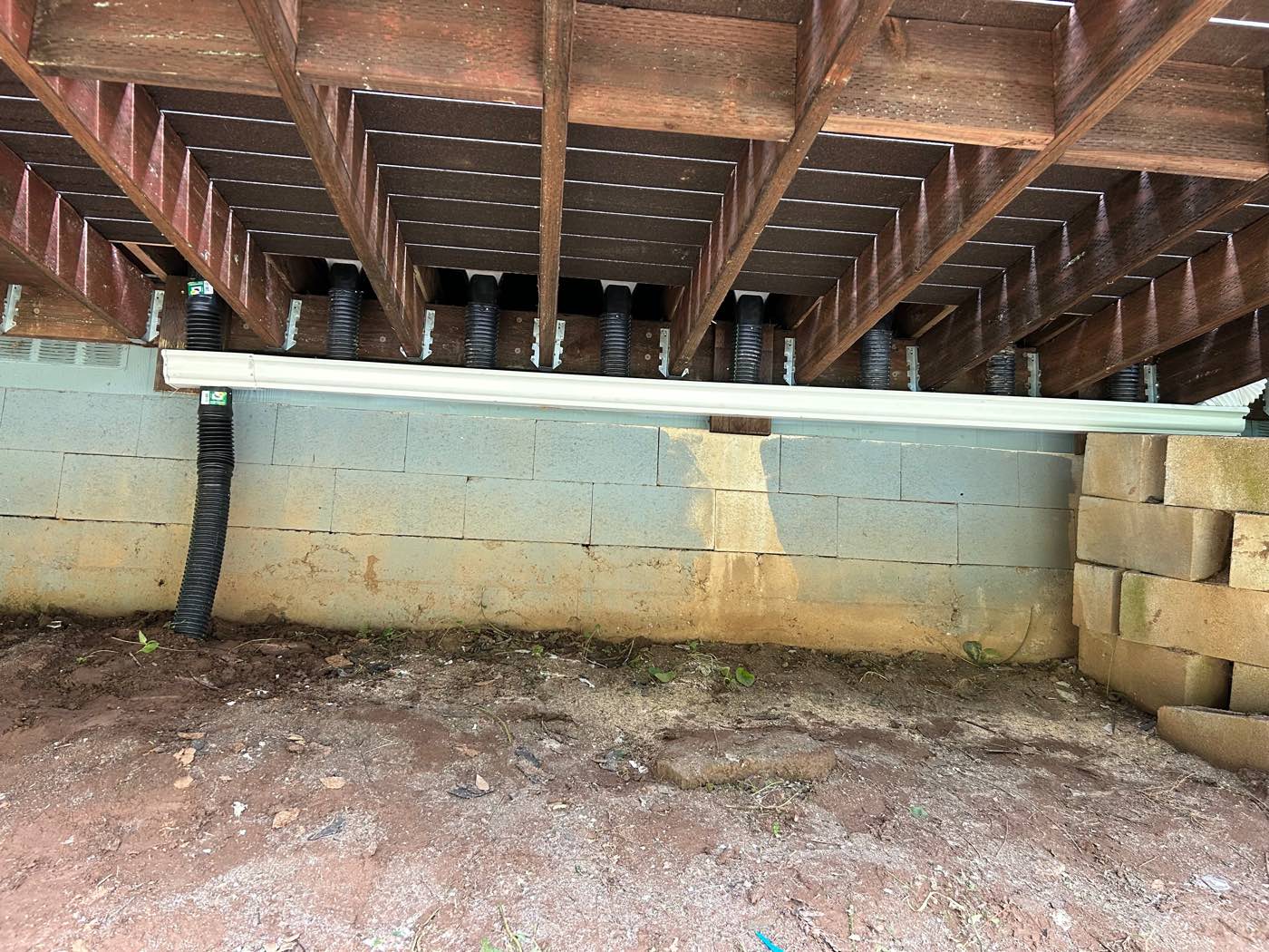 Under-deck drainage system with downspouts and a retaining wall