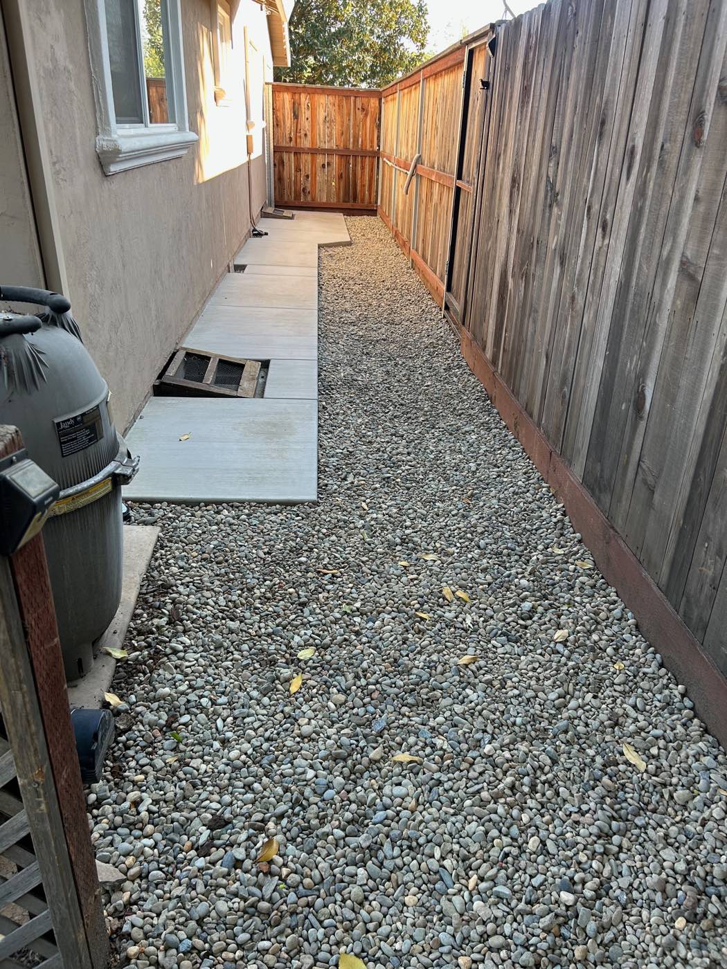 Side yard finished with river rock and pavers along a fence